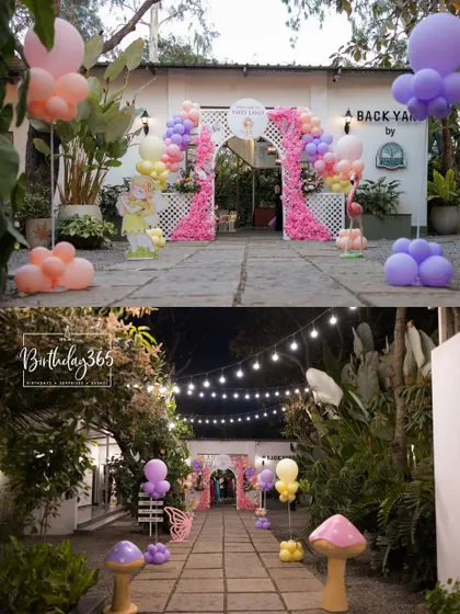 A magical entrance for a fairy-themed party, with a floral balloon arch at dusk and a pathway lit by string lights and mushroom props.