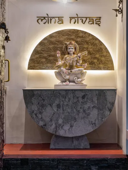 A quaint Saraswati mandir marks the arrival at 'Mina Nivas'. The hand-carved idol from Jaipur rests on a stone veneer pedestal, with a gold-finished halo behind it, creating a peaceful and sanctified entrance.