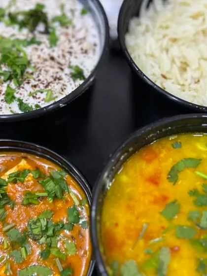 A closer look at the delicious spread of Kadai Paneer, Dal, Rice, and Raita. All dishes are garnished with fresh coriander.
