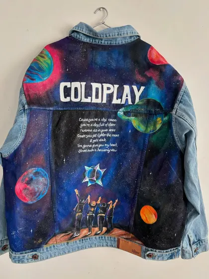This custom-painted denim jacket was created for a client attending a Coldplay concert. The entire back panel is a canvas, featuring a vibrant galaxy scene, the band's silhouette, and iconic lyrics from "A Sky Full of Stars," making it the ultimate piece of fan merchandise.