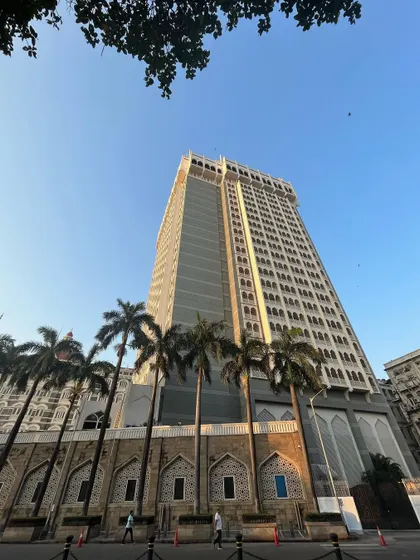 A perspective shot looking up at the Taj Tower from the ground, framed by palm trees.