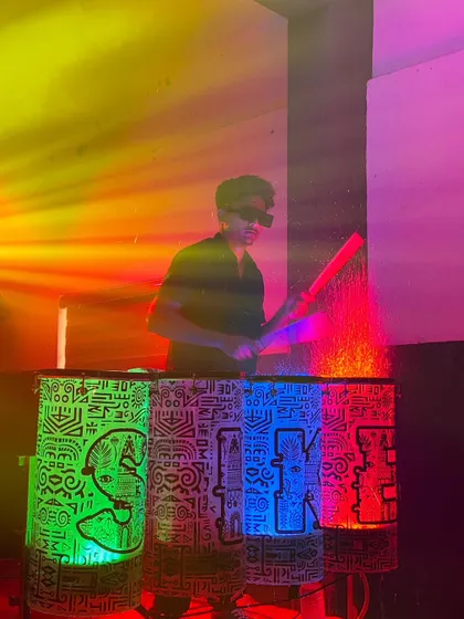 A drummer performing on custom-designed liquid drums, which are illuminated from within and feature unique graphic patterns.