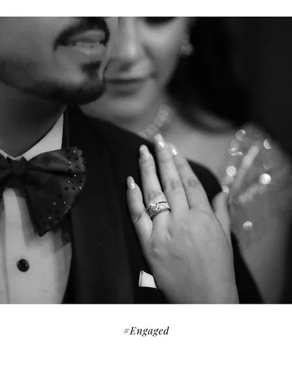 A detailed black and white shot focusing on the engagement ring. The bride's hand rests on the groom's shoulder, symbolizing their new commitment.