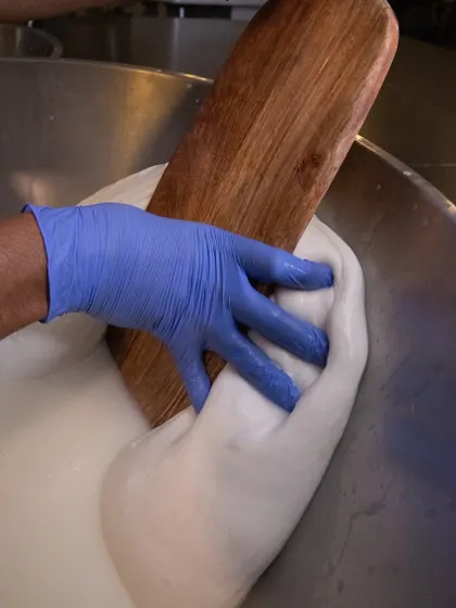 A cheesemaker uses their hands and a wooden board to knead the mozzarella. This hands-on approach allows us to feel when the cheese has reached the perfect elasticity.