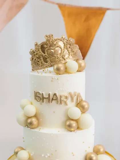 A close-up of the intricate golden crown topper and the elegant gold and white chocolate spheres.
