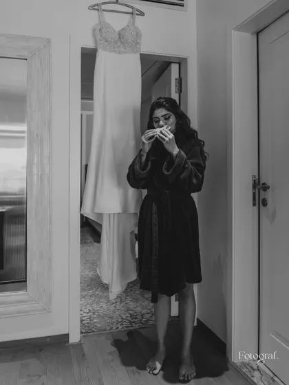A candid, black and white shot of the bride grabbing a quick bite while getting ready, with her wedding dress hanging in the background. A real, unscripted moment.