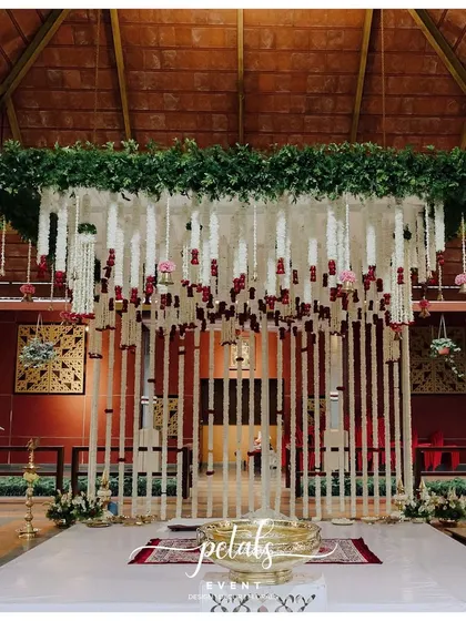 The full view of the mandap stage with the floral curtain backdrop. The clean white stage floor and traditional brass urli create a focal point for the sacred rituals.