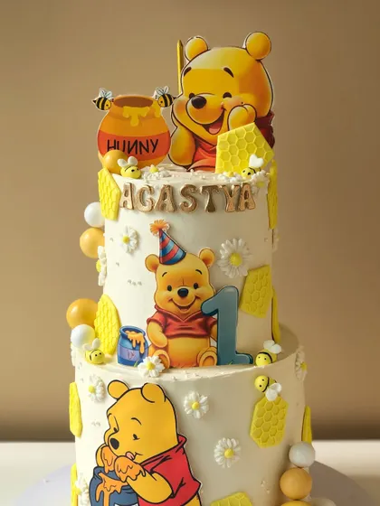 A sweet-as-hunny Winnie the Pooh cake for a first birthday. This two-tiered design is decorated with Pooh and his honey pots, perfect for a classic and heartwarming theme.