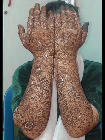 A bride showcasing her full, intricate mehendi design, which covers her hands and arms completely.