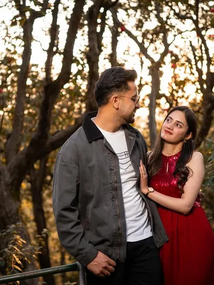 A wider shot of the couple looking at each other, framed by the beautiful texture of the forest trees during golden hour.