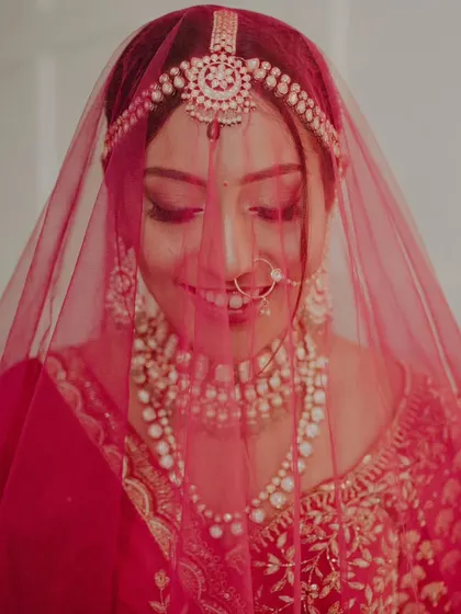 A beautiful shot of the bride under her red veil, her smile soft and radiant.