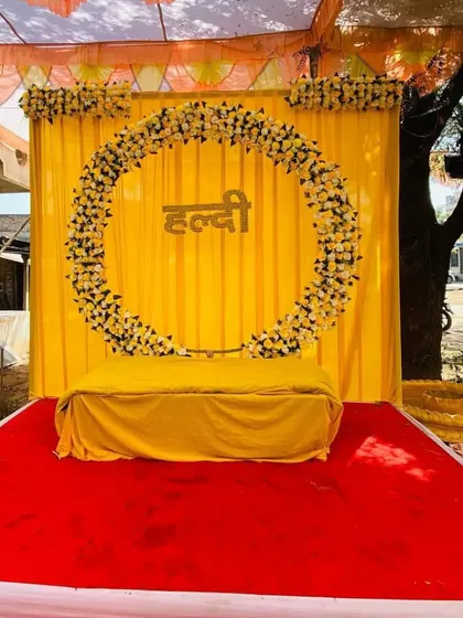 A classic Haldi stage setup with a circular floral arch against a bright yellow backdrop. The stage is covered with a red carpet for a pop of color.