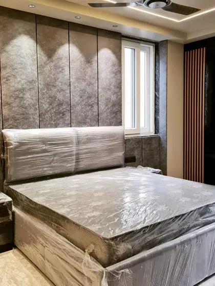 A bedroom in Pitampura just before handover, with a textured grey wallpaper and modern hanging lights, wrapped and ready for the client.