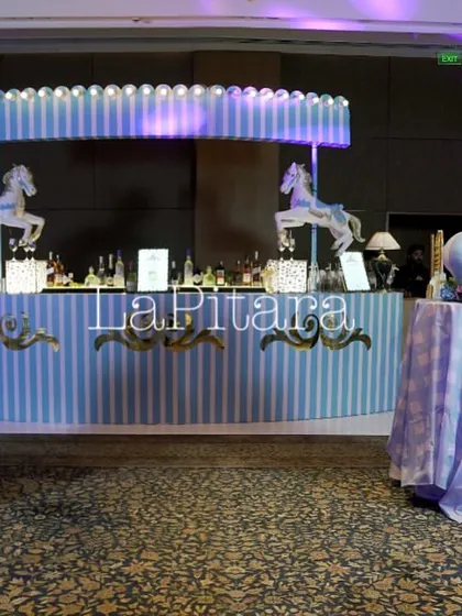 A carnival-themed bar designed for an event at The Oberoi. The setup features classic blue and white stripes and carousel horses, evoking the nostalgic charm of a vintage fairground.