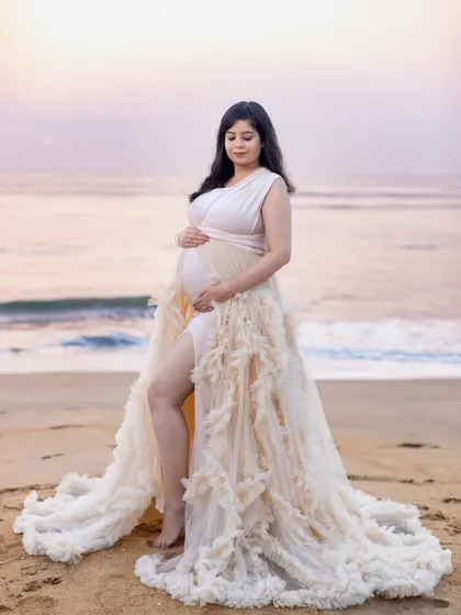 A full-length portrait showcasing the stunning ruffled gown against the calm morning sea. A perfect blend of fashion and maternity photography.