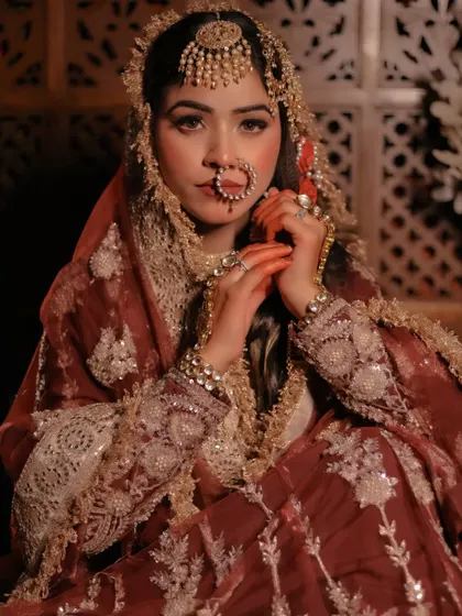 A close-up portrait capturing a vintage, regal aesthetic. The bride's pose and the warm lighting highlight the intricate lace and sequin work on her maroon outfit.
