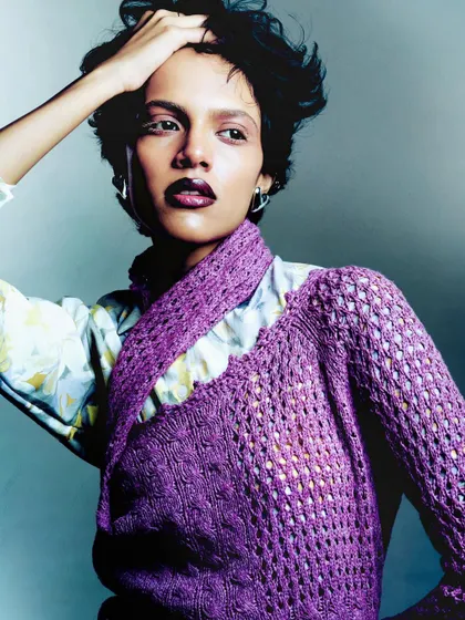 A portrait emphasizing the texture of a purple knit sweater. The model's pose is confident, and the lighting creates a soft, flattering glow.