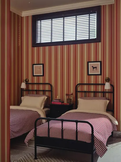 A frontal view of the twin beds in the guest room. The symmetry, high ceilings, and pattern-on-pattern design give this compact room a sense of old-world charm and deliberate composition.