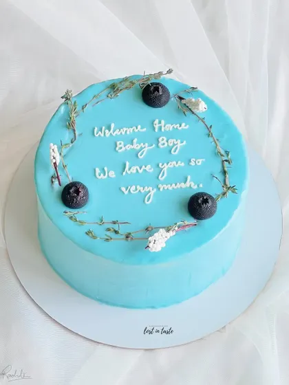 A sweet and simple cake to celebrate a new arrival. This light blue buttercream cake is decorated with delicate herbs and blueberries for a "Welcome Home Baby Boy" party.