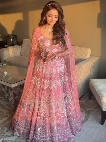 The full view of her magical reception look. The pink cape gown flows beautifully, and her soft, romantic makeup and hair complete the fairy-tale picture.