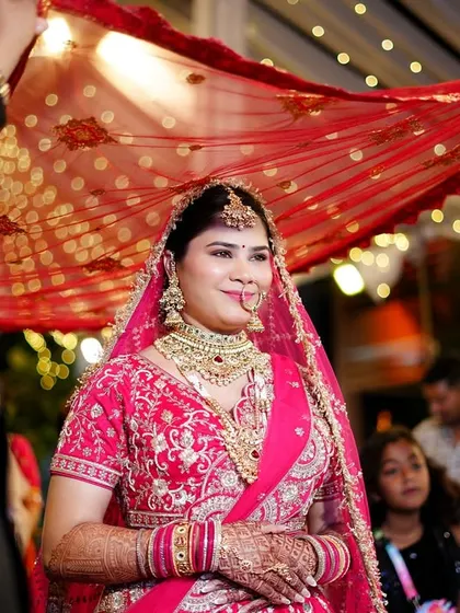The bride being escorted under a traditional red dupatta. This shot captures a beautiful cultural tradition with a focus on the bride's happy expression.