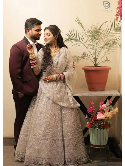 A full-length portrait of a couple in their reception attire, sharing a sweet moment. The bride's silver lehenga and colorful bangles stand out beautifully.