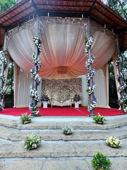 A stunning reception mandap, with a domed structure, elegant drapes, and a backdrop wall completely covered in flowers.
