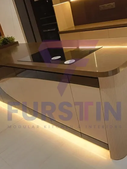 A close-up of the curved kitchen island, showcasing the flawless integration of the induction cooktop into the countertop. The rounded edges soften the design, and the under-island lighting adds a dramatic, floating effect.