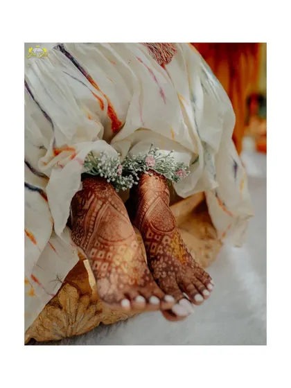 A close-up on the bride's feet, adorned with henna and floral anklets. It’s a beautiful detail shot that captures the traditional and aesthetic elements of the Mehendi ceremony.