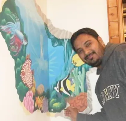 Here I am with a 3D-effect underwater mural I painted. The design makes it look like the wall is broken away, revealing a colorful coral reef with tropical fish. It's a fun and unique way to add depth and imagination to a room.