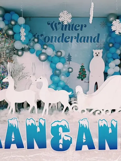 A magical Winter Wonderland theme for a joint birthday party. This setup includes white reindeer cutouts, a snowman, a sleigh, and a blue and silver balloon arch to create a snowy scene.