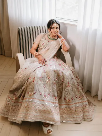 An elegant portrait of a bride seated in a modern chair, her elaborate lehenga spread out beautifully, looking poised and confident.