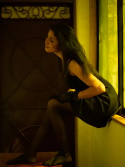 An artistic pose, perched on a windowsill in a black dress, creating a sense of longing and mystery.