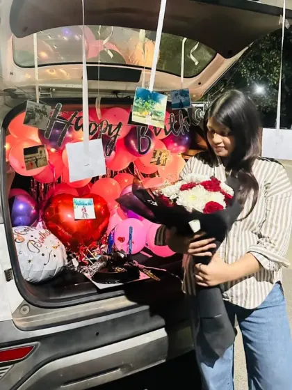 The birthday girl's happy reaction to her personalized car trunk surprise, complete with balloons and a bouquet of flowers.