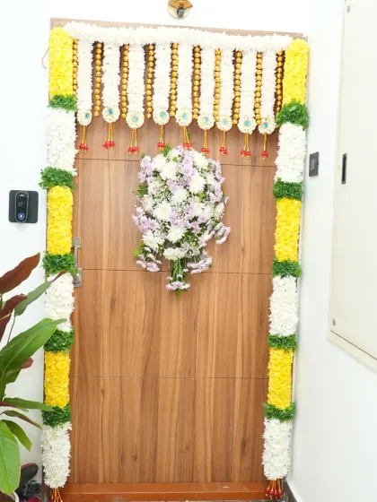 An elegantly decorated main door for a housewarming, featuring jasmine and marigold garlands with a central floral bouquet.
