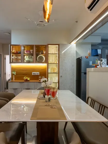 The dining area is strategically placed near the open kitchen, featuring a beautiful marble-top table and a custom-lit crockery unit that adds a touch of elegance and provides ample storage.