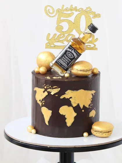 A sophisticated cake for a 50th birthday celebration, combining a love for travel and fine whiskey. This chocolate cake features a hand-painted gold world map, topped with a miniature Jack Daniel's bottle and gold macarons.