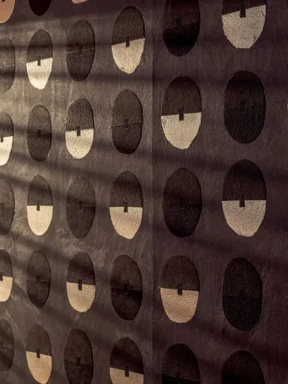 Light and shadow play across the surface of the 'Royal Emblème' wallcovering, highlighting its textured, paper-pulp construction and the graphic quality of its repeating pattern.