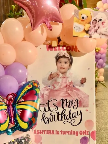 A personalized welcome sign for a butterfly-themed first birthday. The sign features a photo of the birthday girl and is decorated with a matching balloon arrangement.
