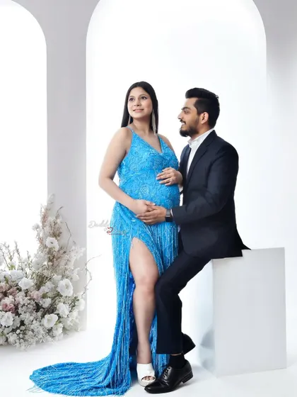 A bright and happy couple's portrait. The mom-to-be wears a stunning, high-slit blue sequin gown, adding a touch of glamour to their studio maternity session.