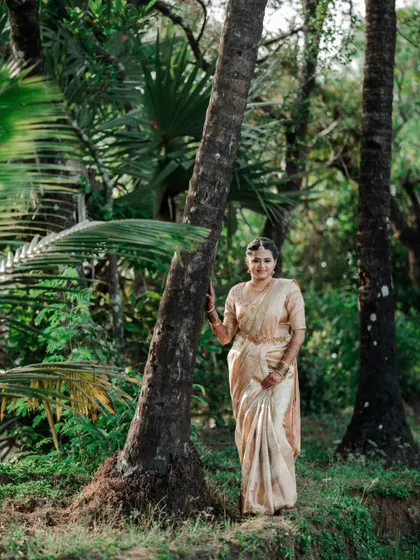 A full-length bridal portrait, with the bride posing elegantly by a tree in a forest setting.