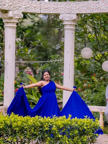 A playful, candid moment from a maternity session. The mom-to-be shows off her flowing blue gown while her partner leans against a pillar in a relaxed pose, capturing a moment of joy and connection.