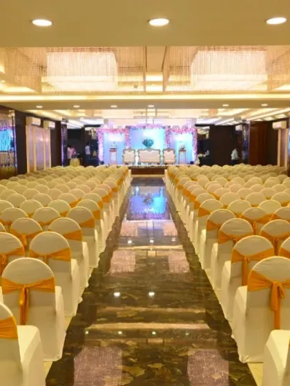 The beautiful interior of Ellora Banquet hall, featuring elegant chandeliers and a long aisle leading to the stage. The seating is arranged neatly with white and yellow covers.