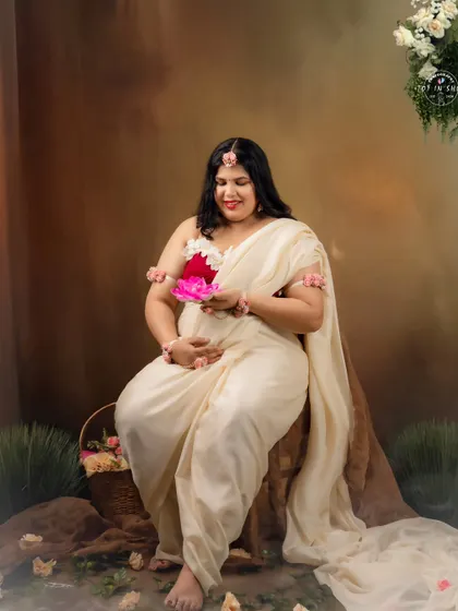 A serene portrait of the mom-to-be seated amidst flowers, holding a lotus, embodying the grace of the mythical character.