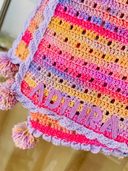 A close up of the name "Adhira" crocheted onto the blanket. We take great care to make the lettering neat and secure, ensuring it becomes a lasting part of this handmade treasure.