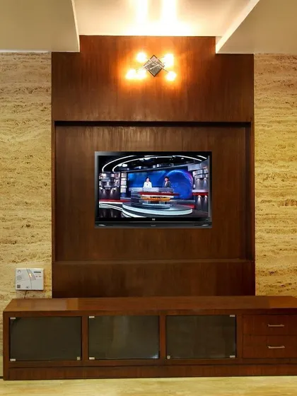 A custom-designed media unit set against a travertine wall. The warm wood of the unit complements the natural stone, creating a sophisticated and integrated solution for entertainment technology.