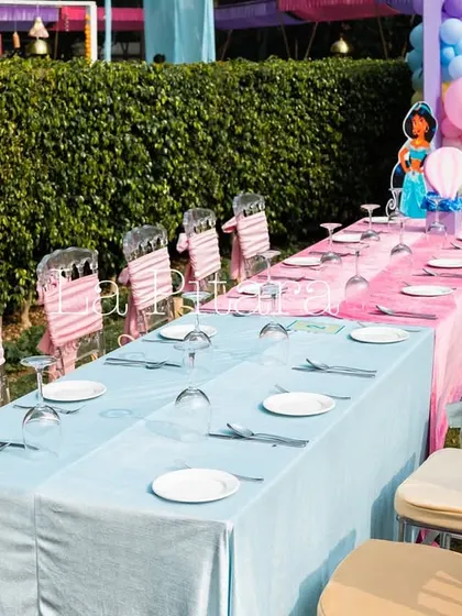The kids' dining table was set up with alternating pink and blue tablecloths. The chairs were decorated with custom sashes, continuing the whimsical Disney theme down to the smallest details.
