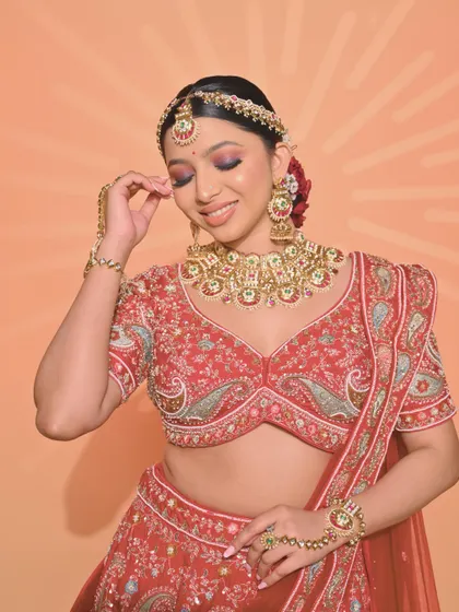 A traditional red lehenga look created by a student, featuring a stunning floral bun and classic bridal makeup.