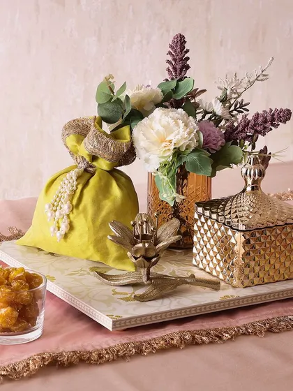The Sunlit Festive hamper brings a golden glow to any celebration. It includes a candle holder, a metal jar with cookies, a flower vase, and a potli of golden berries or choco almonds.