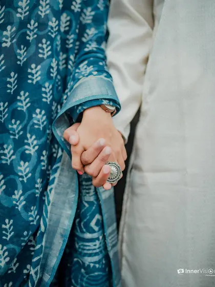 A close-up shot focusing on the couple holding hands. The image highlights the bride's beautiful blue saree and statement ring, symbolizing their connection.